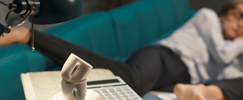 Stressed exhausted businesswoman sleeping on a couch at night, she is surrounded by piles of paperwork, overtime work and deadlines concept